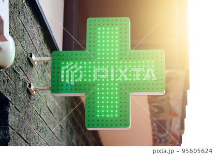 Drugstore signboard on building. Pharmacy green light cross board. Store decoration of downtown. Logo of city dispensary. Sunlight on background. 95605624