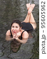 Overweight young woman in black one-piece bathing suit lying down, relaxation in geothermal mineral water in outdoors pool balneotherapy health spa, hot springs resort having balneological properties 95605962