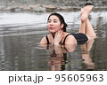Full figured young adult model in black one piece bathing swimsuit lying down and relaxation in mineral water in outdoors pool at spa resort having balneological properties. Woman looking away 95605963