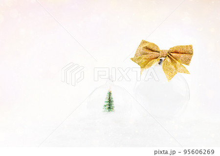 New Year's card background.Close-up.Transparent glass ball with a gold bow lies on the snow on a light bokeh background. New Year's card background.Close-up.Transparent glass ball with a gold bow lies on the snow on a light bokeh background. 95606269