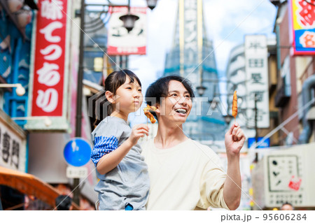 大阪観光で通天閣を背に名物の串かつを食べる親子 大阪観光で通天閣を背に名物の串かつを食べる親子 95606284