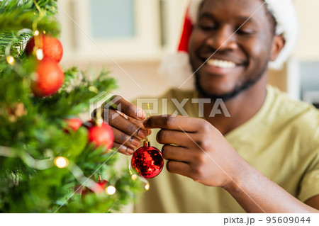 afro american man in Santa hft decorate the christmas tree with a red ball at home 95609044