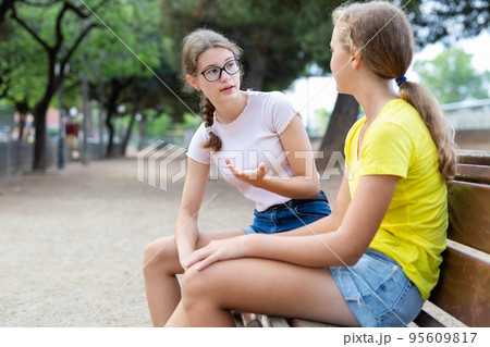 Best friends chatting while sitting on bench in park Best friends chatting while sitting on bench in park 95609817