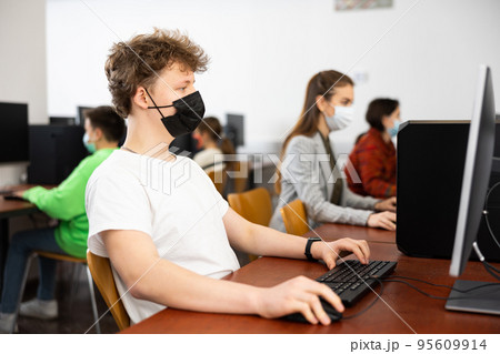 Positive male student wearing face mask working on computer in library. Concept of adult self education during pandemic 95609914