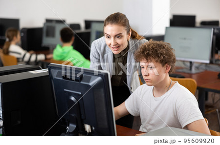 Teacher helping boy to solve computer problem 95609920