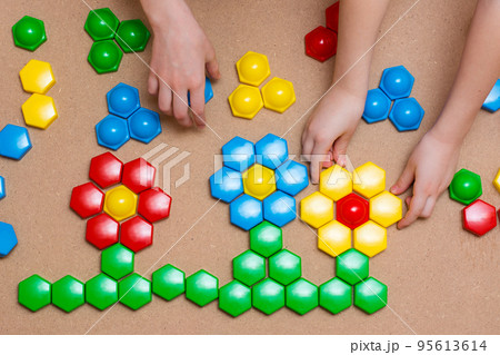 Children's pens folded the details of the colored mosaic into a pattern of flowers on the table. Leisure time for a child in quarantine. Board game. View from above 95613614