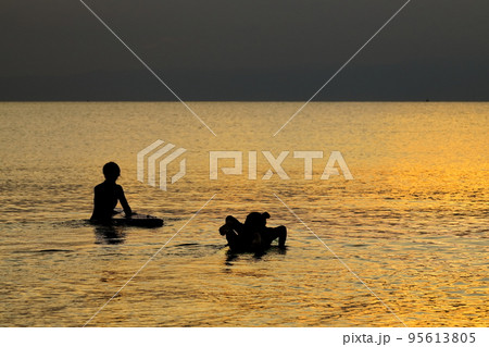 夕暮れの逗子海岸、オレンジ色に染まる海でサーフィンを楽しむ若者たち 95613805