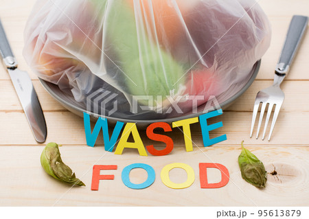 Stop wasting food. A bag of food waste on a plate and cutlery on a wooden table. Food waste concept. 95613879