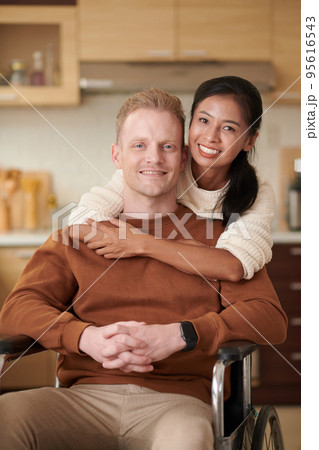 Portrait of happy young man with disability and his pretty girlfriend in kitchen Portrait of happy young man with disability and his pretty girlfriend in kitchen 95616543