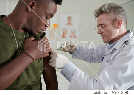 Medical worker injecting vaccine against coronavirus in soulder of Black soldier 95618009