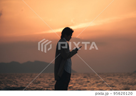 夕方に海辺でスマホを見る男性 夕方に海辺でスマホを見る男性 95620120