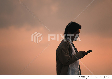 夕方に海辺でスマホを見る男性 95620135