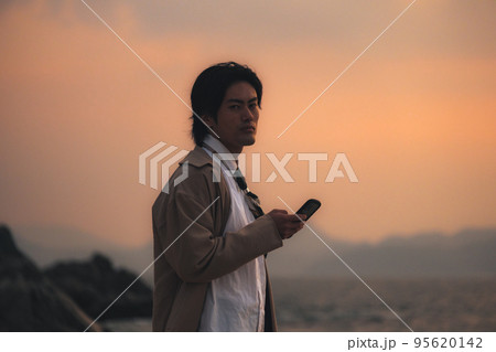 夕方に海辺でスマホを見る男性 夕方に海辺でスマホを見る男性 95620142