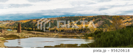 Panoramic autumn landscape. Village and water tower on the shore of the lake. There is a mixed forest on the mountains, the leaves turned yellow. Beautiful sky with clouds. Nature of Eastern Siberia. 95620618