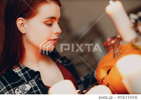 Young woman making Halloween pumpkin Jack-o-lantern with candles. Female hands cutting pumpkins with knife Young woman making Halloween pumpkin Jack-o-lantern with candles. Female hands cutting pumpkins with knife 95625056