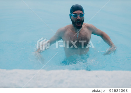 Fit swimmer male training swim in open winter swimming pool with fog. Geothermal outdoor spa health concept. 95625068