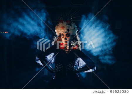 Woman with mexican skull halloween makeup in dark with backlight rays. Day of the dead aka Dia de los Muertos and halloween concept. 95625080