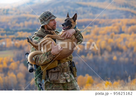 Soldier is holding his faithful friend in his arms - a dog of the Malinois breed. Soldier is holding his faithful friend in his arms - a dog of the Malinois breed. 95625162