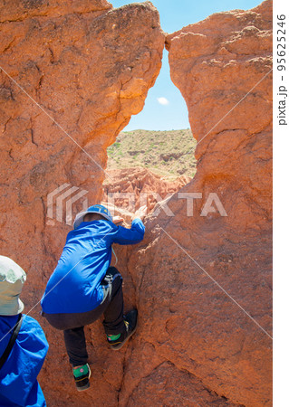 A boy in sports clothes and climbing over a rock made of orange clay against the background of the sky and the green horizon.Sports healthy childhood. 95625246