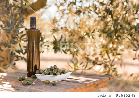 green olives and oil on table in olive grove 95625248
