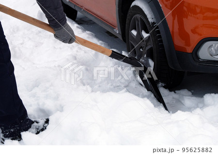 Man with shovel is brushing snow around car after snow storm. Shovel in hand. Winter problems of car drivers. 95625882