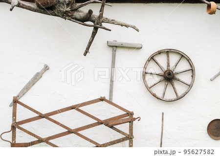 An old wooden wall of a house in the village and ancient cart wheels, tools, etc 95627582