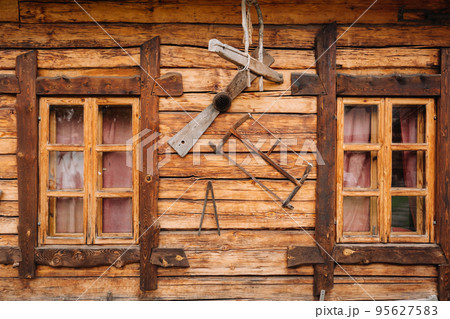 An old wooden wall of a house with windows in the village and tools hanging 95627583
