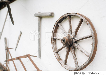 An old wooden wall of a house in the village and ancient cart wheels, tools, etc An old wooden wall of a house in the village and ancient cart wheels, tools, etc 95627730