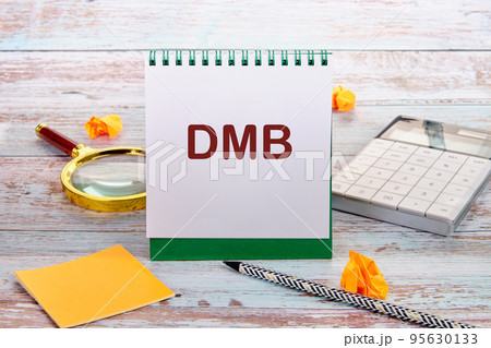 DMB text is written on a notebook sheet, next to a calculator, stickers, pencil, magnifying glass 95630133