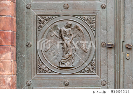 Angel carving on church doors in Berlin, Germany. Detail of the metallic panel on the temple doorway, entrance to the church. Angel carving on church doors in Berlin, Germany. Detail of the metallic panel on the temple doorway, entrance to the church. 95634512