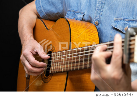 Guitarist playing acoustic guitar on black background, selective focus. A man playing acoustic guitar Guitarist playing acoustic guitar on black background, selective focus. A man playing acoustic guitar 95635447