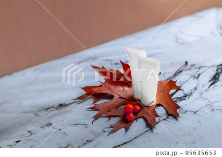 White tubes of cream or lotion without markings with autumn leaves and red rowan berries. A bottle for a template of cosmetics. Autumn skin care, marble background White tubes of cream or lotion without markings with autumn leaves and red rowan berries. A bottle for a template of cosmetics. Autumn skin care, marble background 95635653