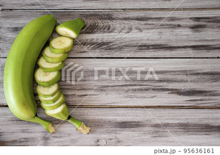 Green bananas on a wooden background. Whole banana and cut into circles. Flat lay, top view, copy space Green bananas on a wooden background. Whole banana and cut into circles. Flat lay, top view, copy space 95636161