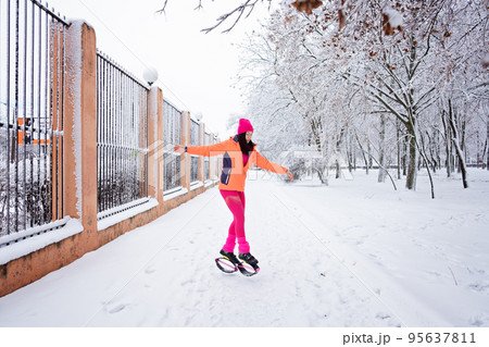 Winter workout, exercising in cold weather. Winter fitness Trening kangoo jumps. Sporty woman in sportswear and kangoo jump shoes jumping in winter snowy park, forest. 95637811