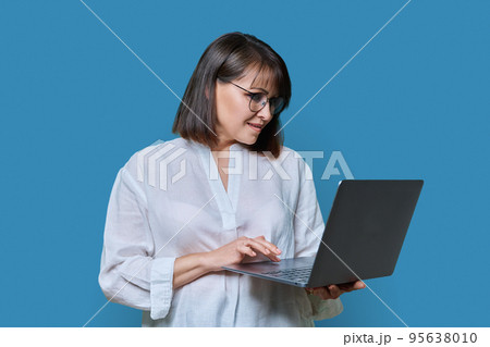 Smiling attractive mature woman with laptop on blue background Smiling attractive mature woman with laptop on blue background 95638010