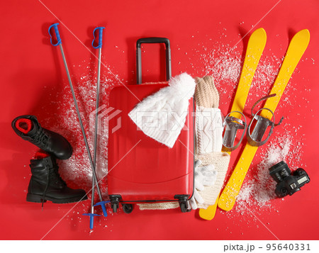 Suitcase with warm clothes, camera and skis on red background, flat lay. Winter vacation Suitcase with warm clothes, camera and skis on red background, flat lay. Winter vacation 95640331