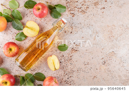 Apple cider vinegar in a glass bottle and fresh apples with leaves on beige concrete background, top view, flat lay 95640645