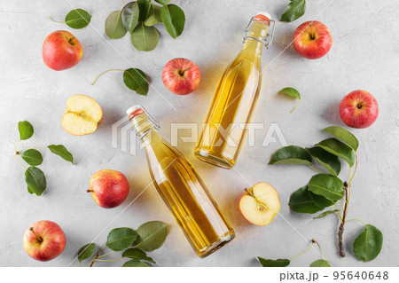 Apple cider vinegar in a two glass bottles and fresh apples with leaves on light background, top view, flat lay 95640648