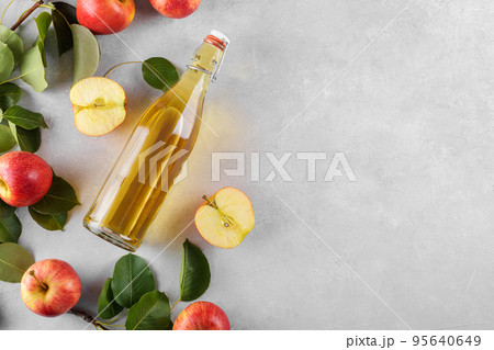 Apple cider vinegar in a glass bottle and fresh apples with leaves on light background, top view, flat lay Apple cider vinegar in a glass bottle and fresh apples with leaves on light background, top view, flat lay 95640649