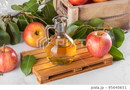 Apple cider vinegar in a glass bottle and fresh apples with leaves on light background Apple cider vinegar in a glass bottle and fresh apples with leaves on light background 95640651