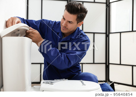 Professional plumber working with toilet bowl in bathroom 95640854
