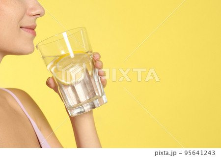 Young woman drinking lemon water on yellow background, closeup. Space for text 95641243