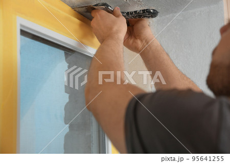 Man plastering window area with putty knife indoors, closeup. Interior repair Man plastering window area with putty knife indoors, closeup. Interior repair 95641255