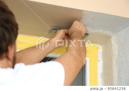 Man plastering window area with putty knife indoors, closeup. Interior repair 95641256
