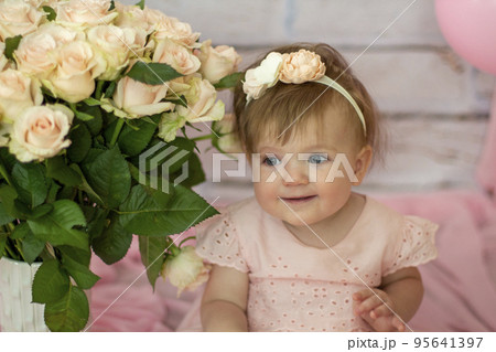 Pretty small girl with roses in beautiful dress sits and looks dreamy, beauty and fashion concept, indoor portrait against the backdrop of brick wall close-up. Beautiful little girl model . 95641397
