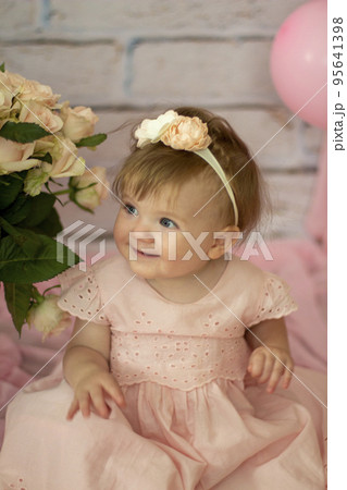Pretty small girl with roses in beautiful dress sits and looks dreamy, beauty and fashion concept, indoor portrait against the backdrop of brick wall close-up. Beautiful little girl model . 95641398