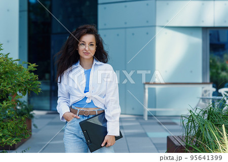 Successful beautiful business woman in suit with document walking to the meeting near modern office building. Successful beautiful business woman in suit with document walking to the meeting near modern office building. 95641399