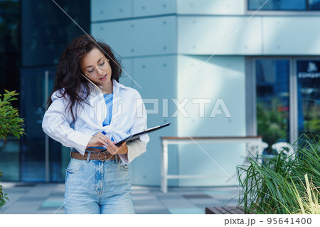Successful beautiful business woman in suit with document walking to the meeting near modern office building. Successful beautiful business woman in suit with document walking to the meeting near modern office building. 95641400