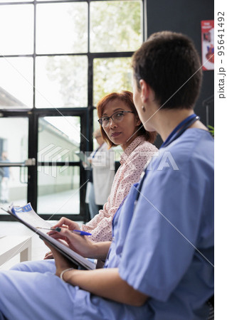 Medical asisstant filling in clinical report papers with senior patient, doing healthcare examination hospital waiting room. Nurse writing checkup form documents before appointment. 95641492