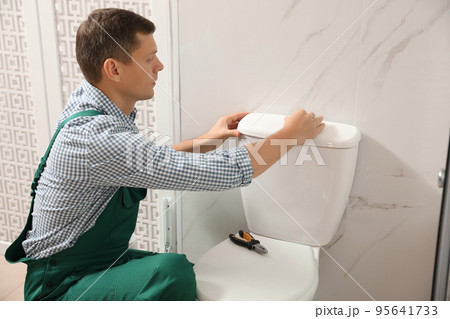 Professional plumber repairing toilet bowl in bathroom 95641733